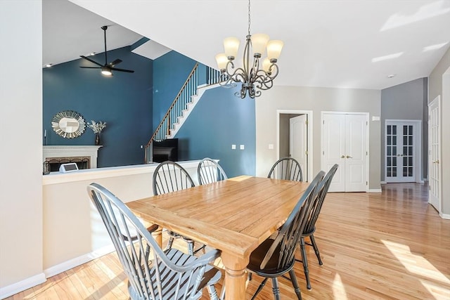 dining space featuring baseboards, a fireplace, light wood finished floors, and ceiling fan with notable chandelier