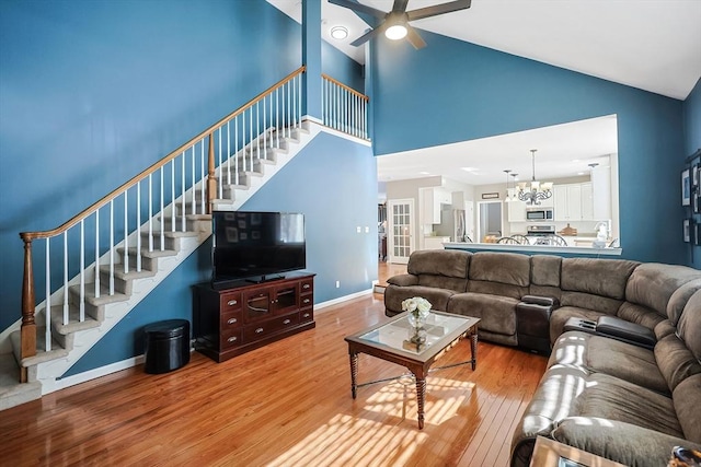 living area featuring ceiling fan with notable chandelier, stairway, baseboards, and light wood-style floors