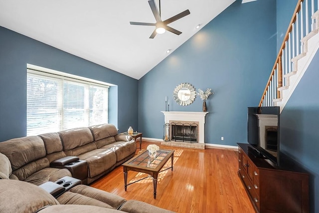 living area with a fireplace with raised hearth, ceiling fan, light wood finished floors, and stairs