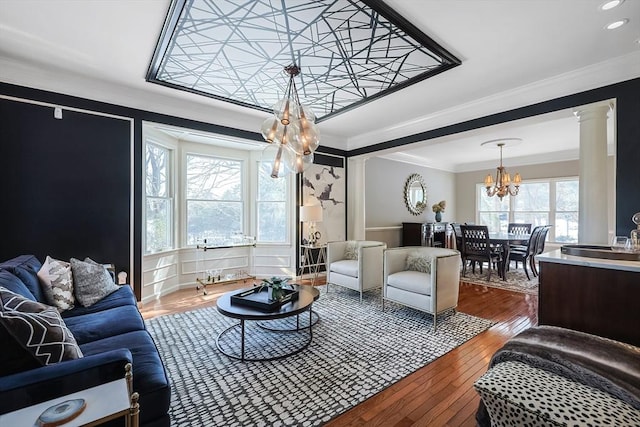 living room featuring decorative columns, ornamental molding, wood finished floors, an inviting chandelier, and recessed lighting