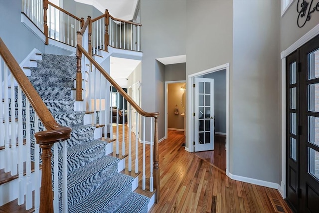 foyer entrance with wood finished floors, visible vents, a towering ceiling, stairs, and baseboards