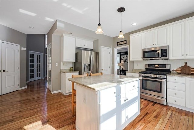 kitchen featuring stainless steel appliances, white cabinets, a kitchen island, and light stone counters