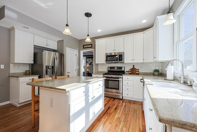 kitchen with a center island, decorative light fixtures, stainless steel appliances, white cabinetry, and a sink