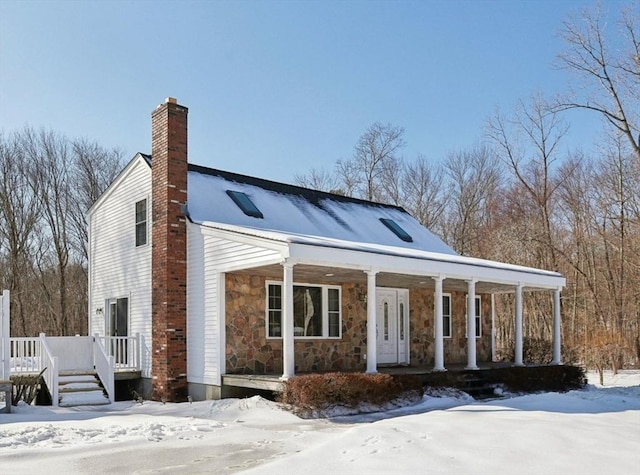 view of front facade with covered porch, stone siding, and a chimney