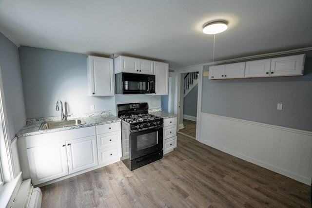 kitchen featuring a wainscoted wall, light wood-style floors, white cabinets, a sink, and black appliances