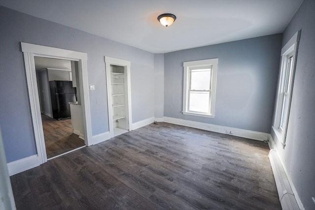 unfurnished bedroom with dark wood-style floors, visible vents, baseboards, and freestanding refrigerator