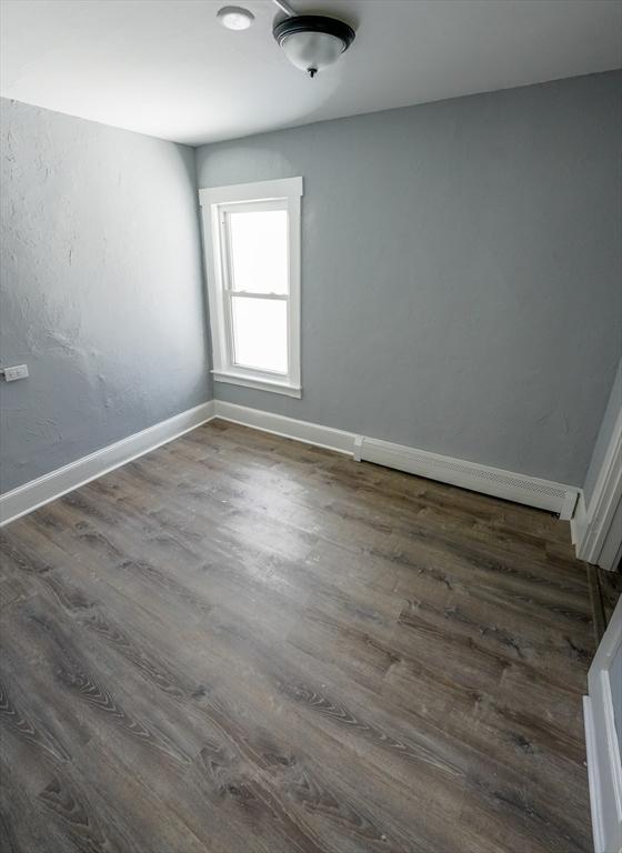 spare room with a baseboard radiator, baseboards, and dark wood finished floors