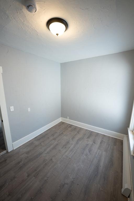 unfurnished room featuring a textured ceiling, dark wood-type flooring, and baseboards