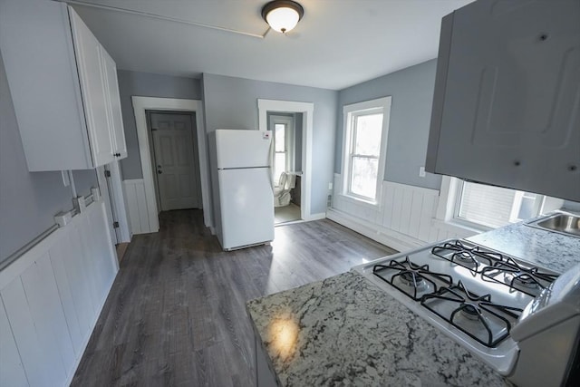 kitchen with a wainscoted wall, white appliances, dark wood-style flooring, white cabinets, and light stone countertops