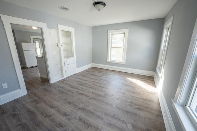 unfurnished bedroom with visible vents, wood finished floors, freestanding refrigerator, and baseboards