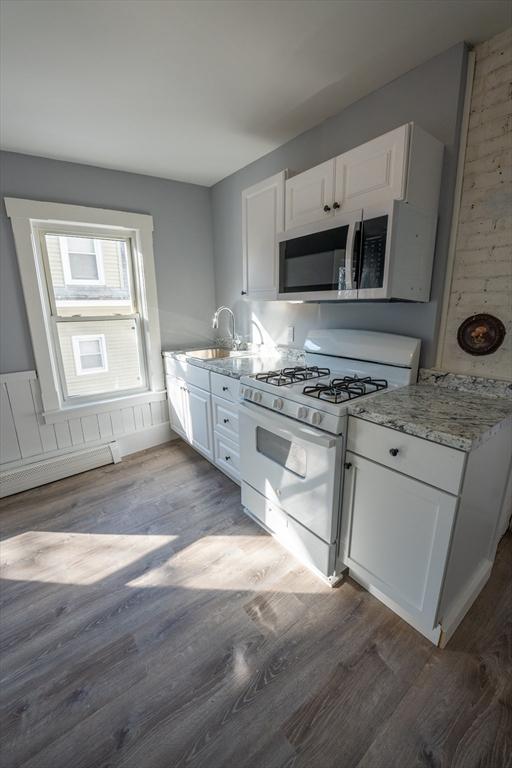 kitchen with a sink, gas range gas stove, wood finished floors, and white cabinetry