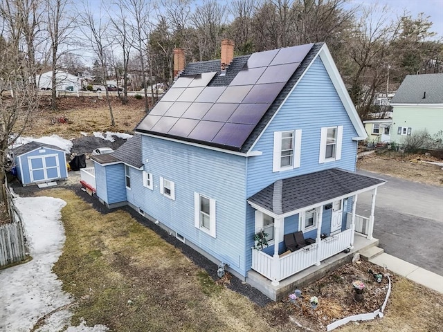 rear view of property featuring roof mounted solar panels, a porch, a shed, roof with shingles, and an outdoor structure