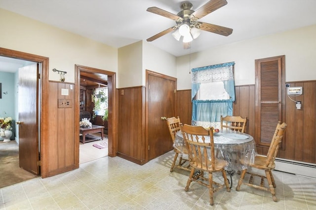 dining space with baseboard heating, wainscoting, wood walls, and ceiling fan