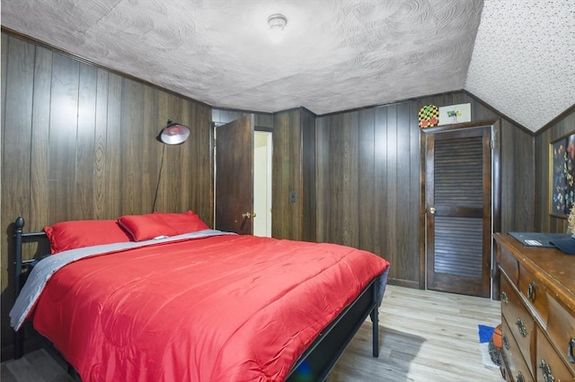 bedroom with lofted ceiling, wooden walls, wood finished floors, and a textured ceiling