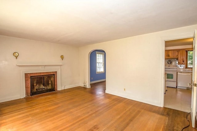 112 Harmon Ave, Springfield, MA 01118 - unfurnished living room featuring arched walkways, wood finished floors, healthy amount of natural light, and a brick fireplace