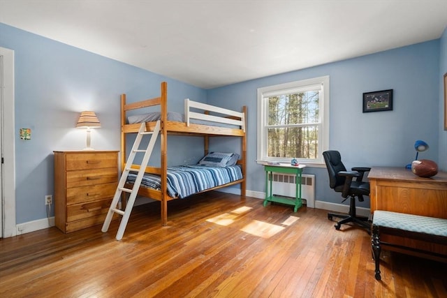 bedroom with radiator heating unit, hardwood / wood-style floors, an office area, and baseboards