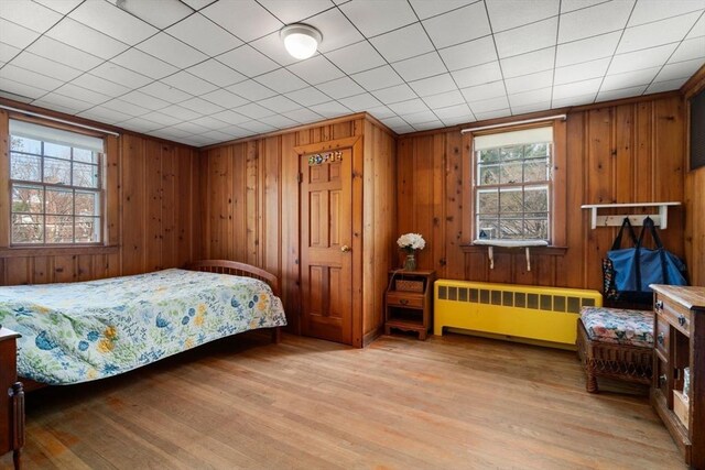 bedroom featuring radiator, multiple windows, light wood-style floors, and wooden walls