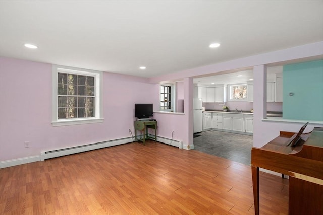 unfurnished living room featuring light wood-style flooring, baseboard heating, a sink, and recessed lighting