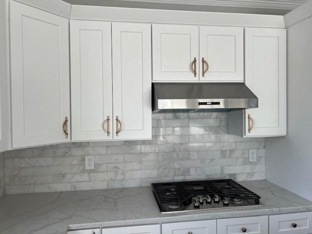 kitchen with stainless steel gas cooktop, light stone countertops, white cabinets, wall chimney range hood, and backsplash