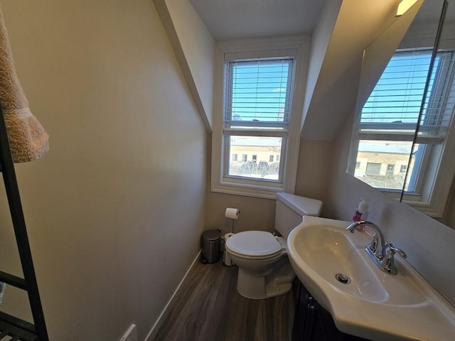 half bathroom with a sink, toilet, baseboards, and wood finished floors