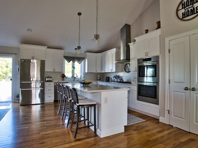 kitchen featuring dark hardwood / wood-style floors, stainless steel appliances, white cabinets, a center island, and wall chimney range hood