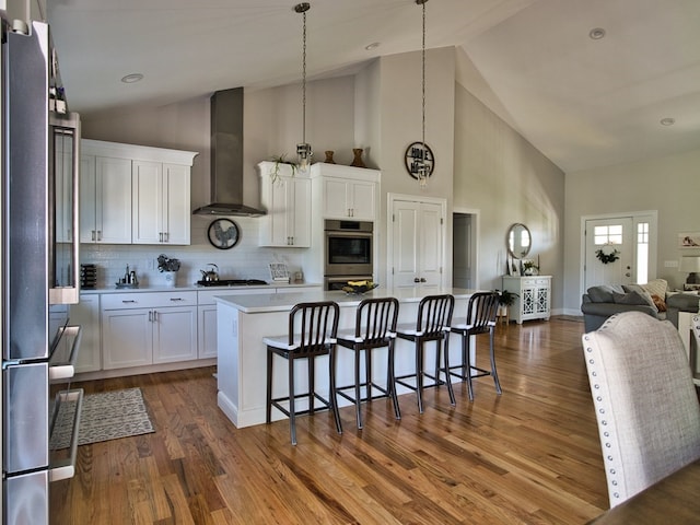 kitchen with dark hardwood / wood-style flooring, a kitchen breakfast bar, wall chimney range hood, and white cabinets