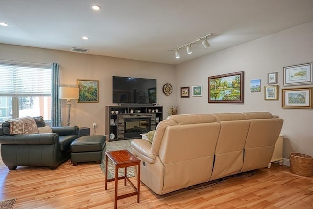 living area featuring light wood finished floors, recessed lighting, visible vents, and a glass covered fireplace