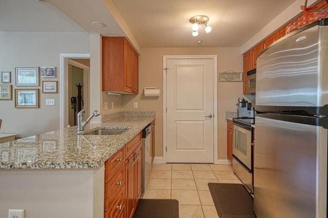 kitchen featuring light tile patterned floors, appliances with stainless steel finishes, brown cabinets, light stone countertops, and a sink