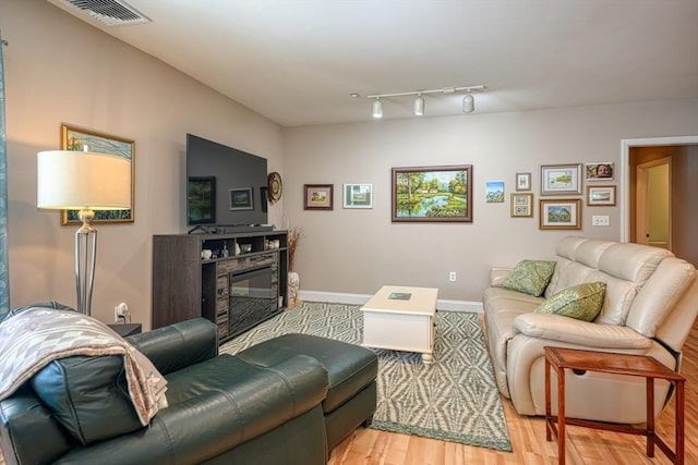 living room featuring light wood finished floors, a glass covered fireplace, visible vents, and baseboards