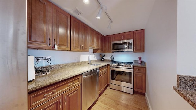 kitchen with sink, rail lighting, stainless steel appliances, light stone counters, and light hardwood / wood-style floors