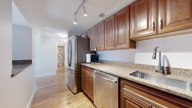 kitchen with light stone countertops, sink, light hardwood / wood-style floors, track lighting, and appliances with stainless steel finishes