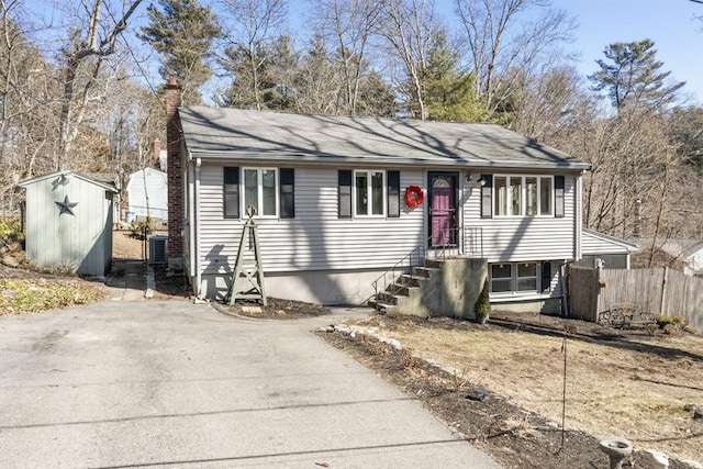 view of front of property featuring an outbuilding, aphalt driveway, a shed, fence, and a chimney