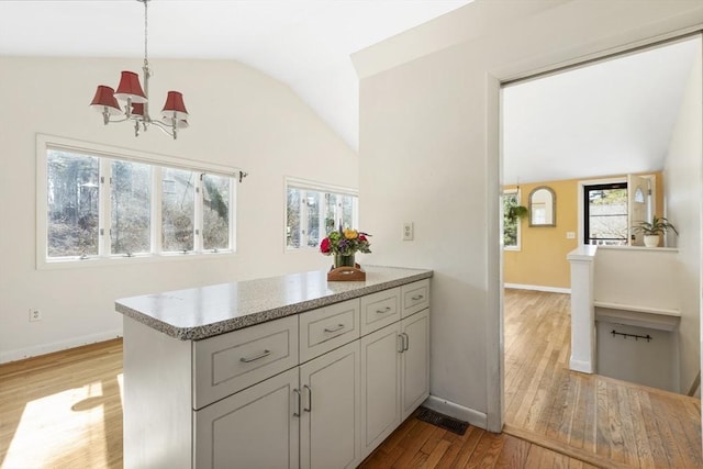 kitchen with light wood-style flooring, a peninsula, baseboards, and vaulted ceiling