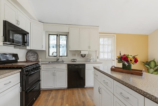 kitchen with black appliances, light wood-type flooring, vaulted ceiling, white cabinetry, and a sink