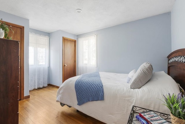 bedroom featuring baseboards, a textured ceiling, and light wood finished floors