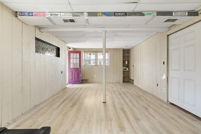 below grade area with visible vents, a drop ceiling, wooden walls, and wood finished floors