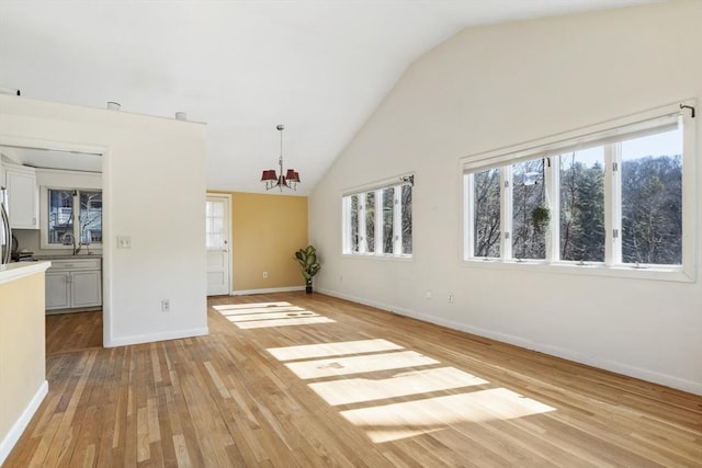 interior space with baseboards, a sink, vaulted ceiling, light wood-style floors, and a chandelier