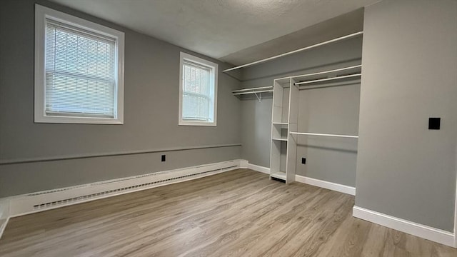 unfurnished bedroom with a closet, baseboard heating, baseboards, and wood finished floors