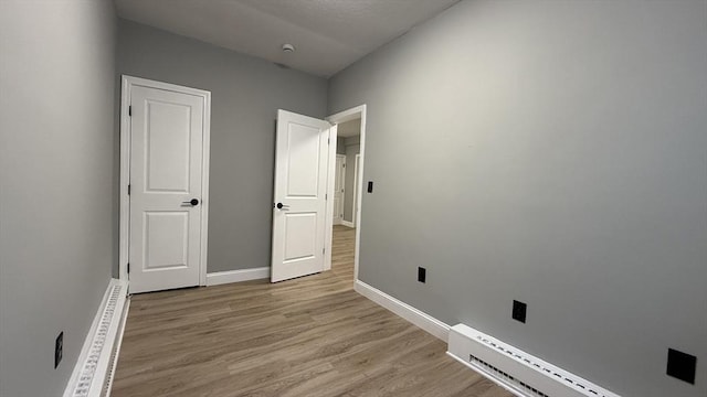 empty room featuring light wood finished floors, baseboard heating, and baseboards