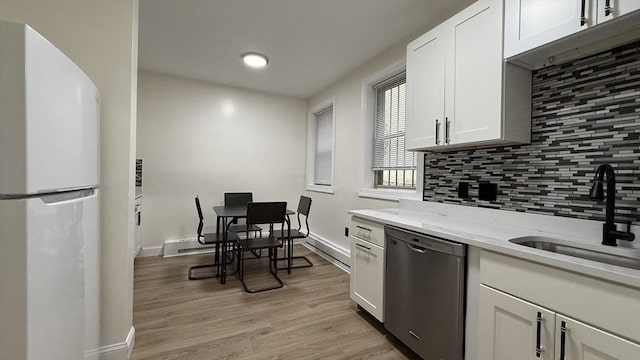 kitchen featuring freestanding refrigerator, a sink, decorative backsplash, white cabinets, and stainless steel dishwasher