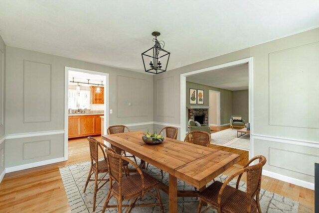 759 Williams St, Longmeadow, MA 01106 - dining room featuring a decorative wall, light wood-style floors, a chandelier, and a brick fireplace