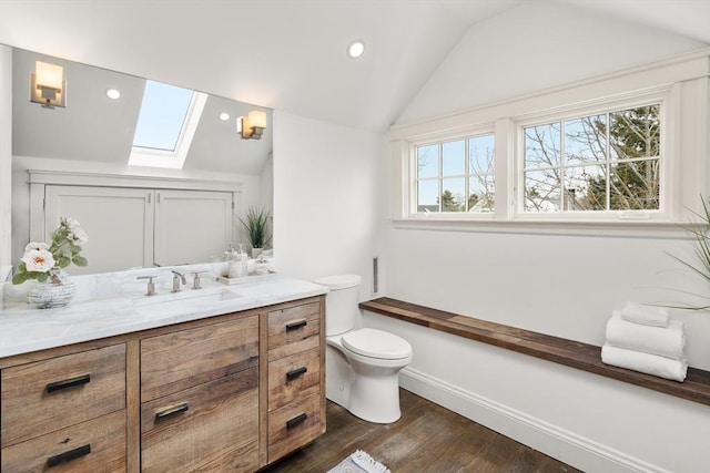 bathroom with recessed lighting, toilet, vanity, wood finished floors, and vaulted ceiling with skylight