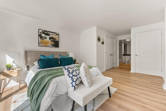 bedroom featuring baseboards, light wood finished floors, and ensuite bathroom