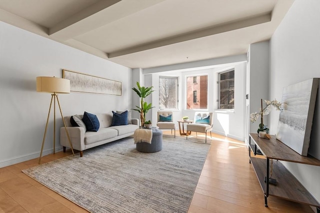 living area featuring baseboards, beamed ceiling, and light wood finished floors