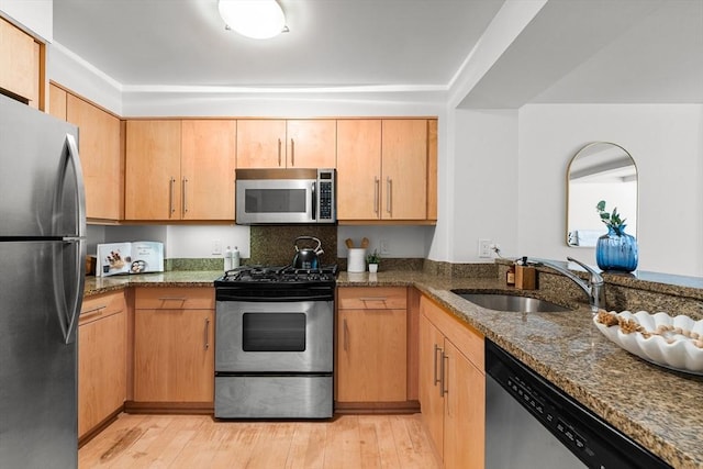 kitchen featuring stainless steel appliances, dark stone counters, a sink, and light wood-style flooring