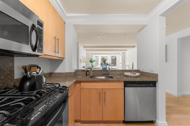 kitchen with stainless steel appliances, light wood-style flooring, light brown cabinetry, a sink, and dark stone countertops