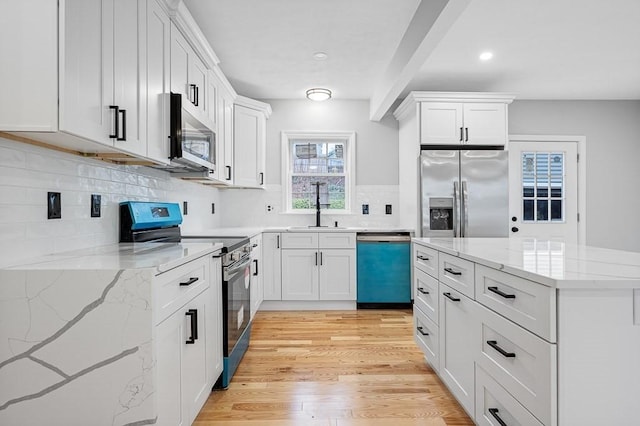 kitchen with tasteful backsplash, light wood-style flooring, white cabinets, stainless steel appliances, and a sink
