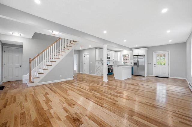 unfurnished living room featuring stairs, light wood-style flooring, baseboards, and a sink