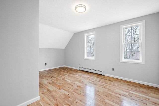 additional living space with vaulted ceiling, light wood-style flooring, a baseboard heating unit, and baseboards