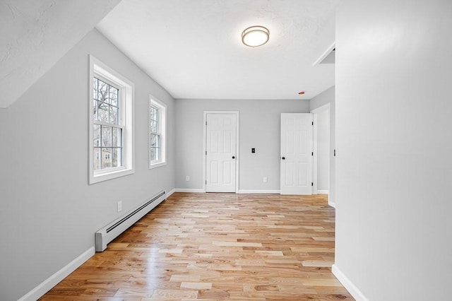 unfurnished bedroom featuring baseboard heating, light wood finished floors, and baseboards